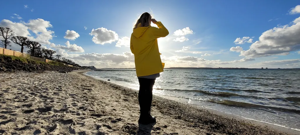 Lea Jansen im gelben Mantel am Ostseestrand, mit dem Blick aufs Wasser